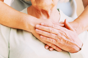 Older woman holding nurses hand on upper chest