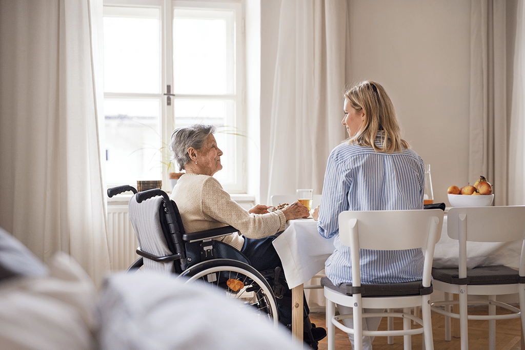 senior woman in wheelchair with a health visitor sitting at the table at home