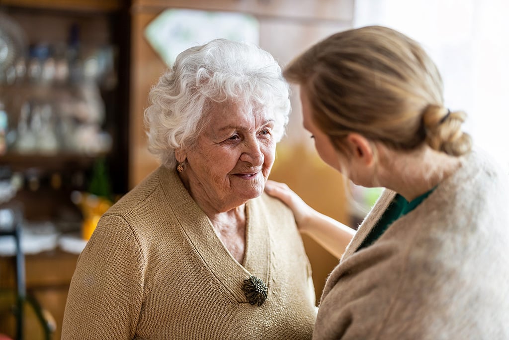 woman placing hand on shoulder of and talking with woman with dementia