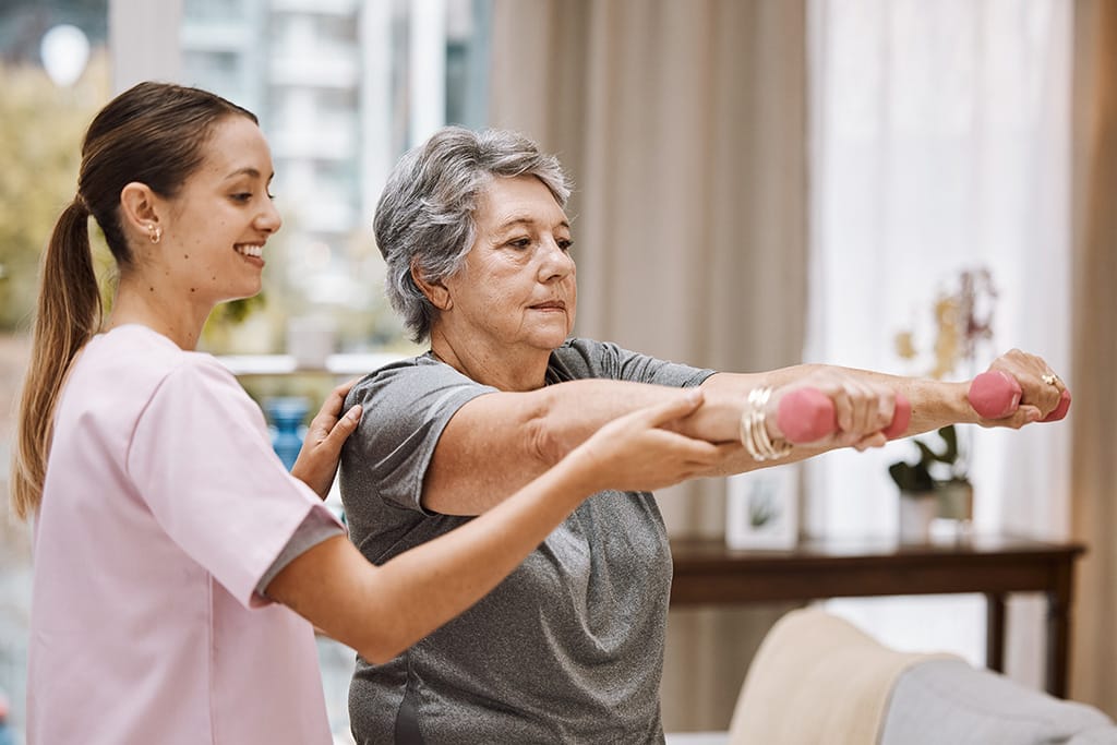 Women helping senior woman with dumbbells in senior living home