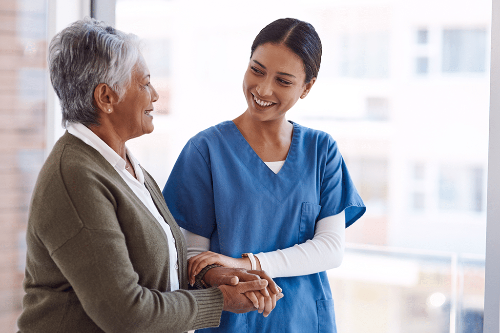 caregiver holding hands with senior woman inside care facility