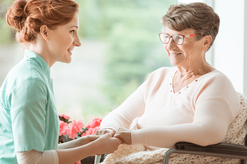 Compassionate nurse holding the hands of an elderly woman while both are sitting down and looking at each other