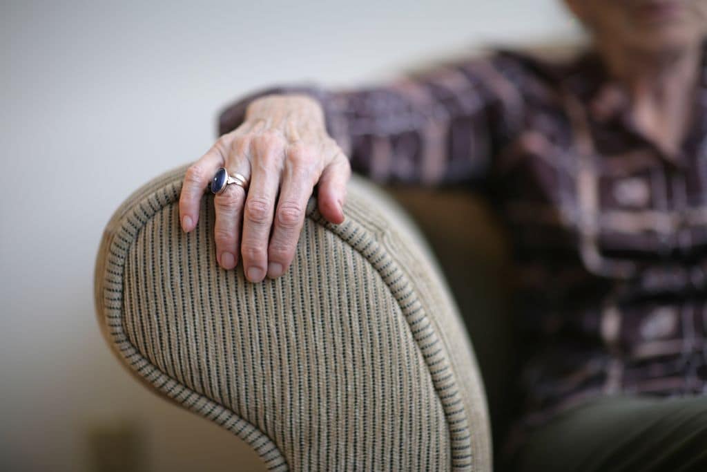 elderly woman rests her arm on the arm of a sofa